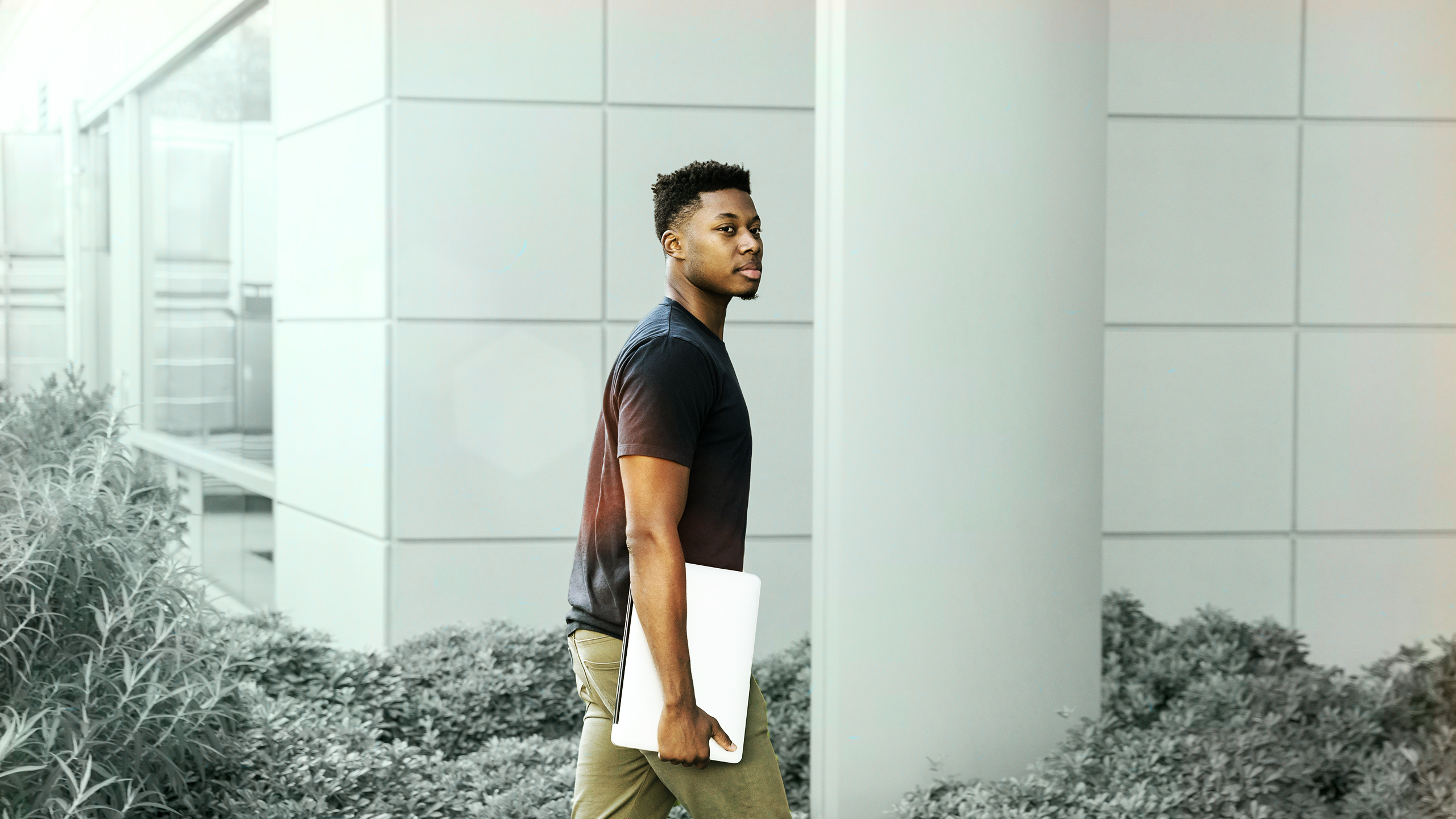 man holding laptop walking towards building