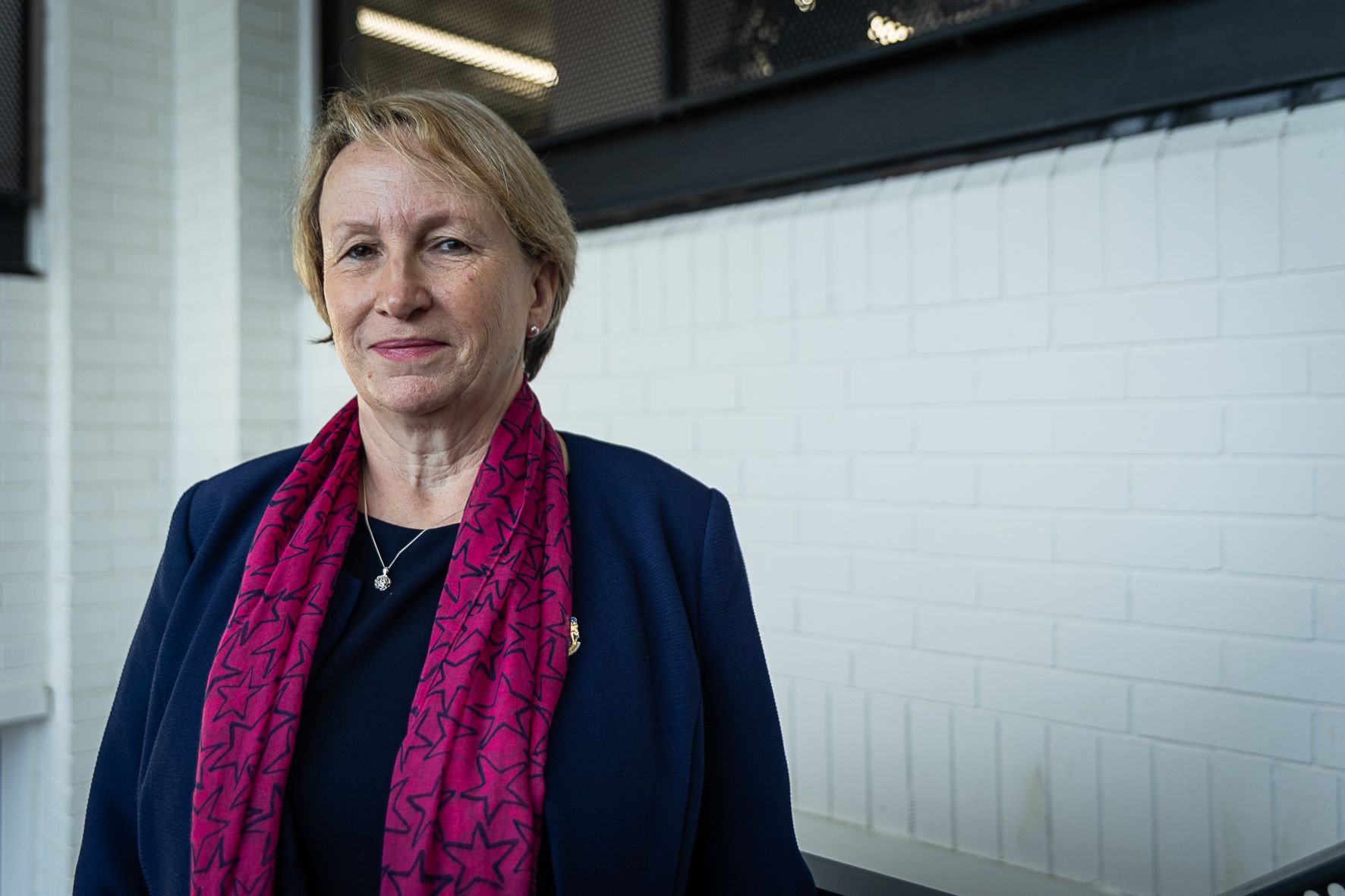 Charlotte Beardmore, pictured smiling with a white wall as a backdrop. Charlotte is wearing a dark blue blazer, diamond necklace and her SOR brooche