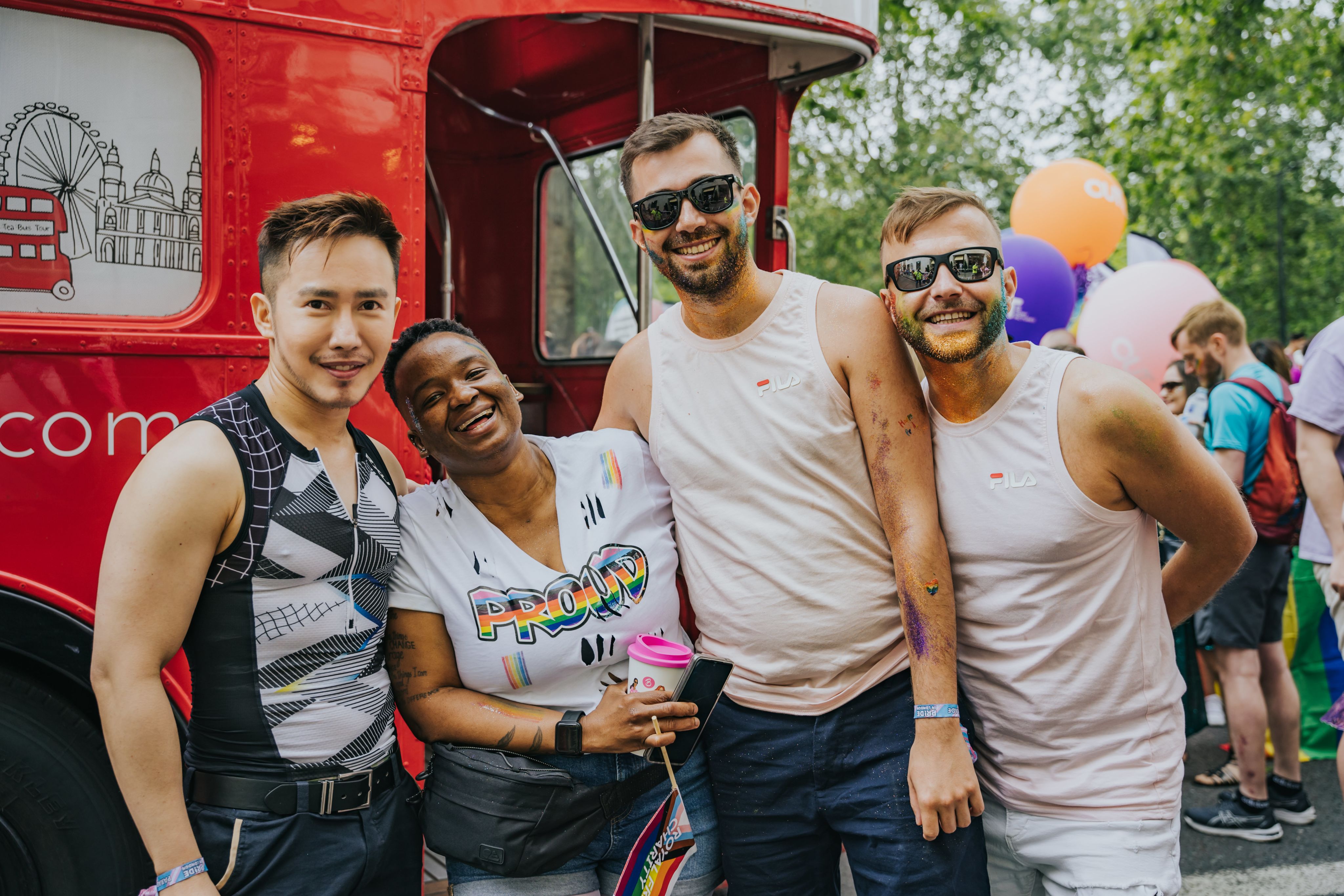 Four people showing their support for pride next to the london bus