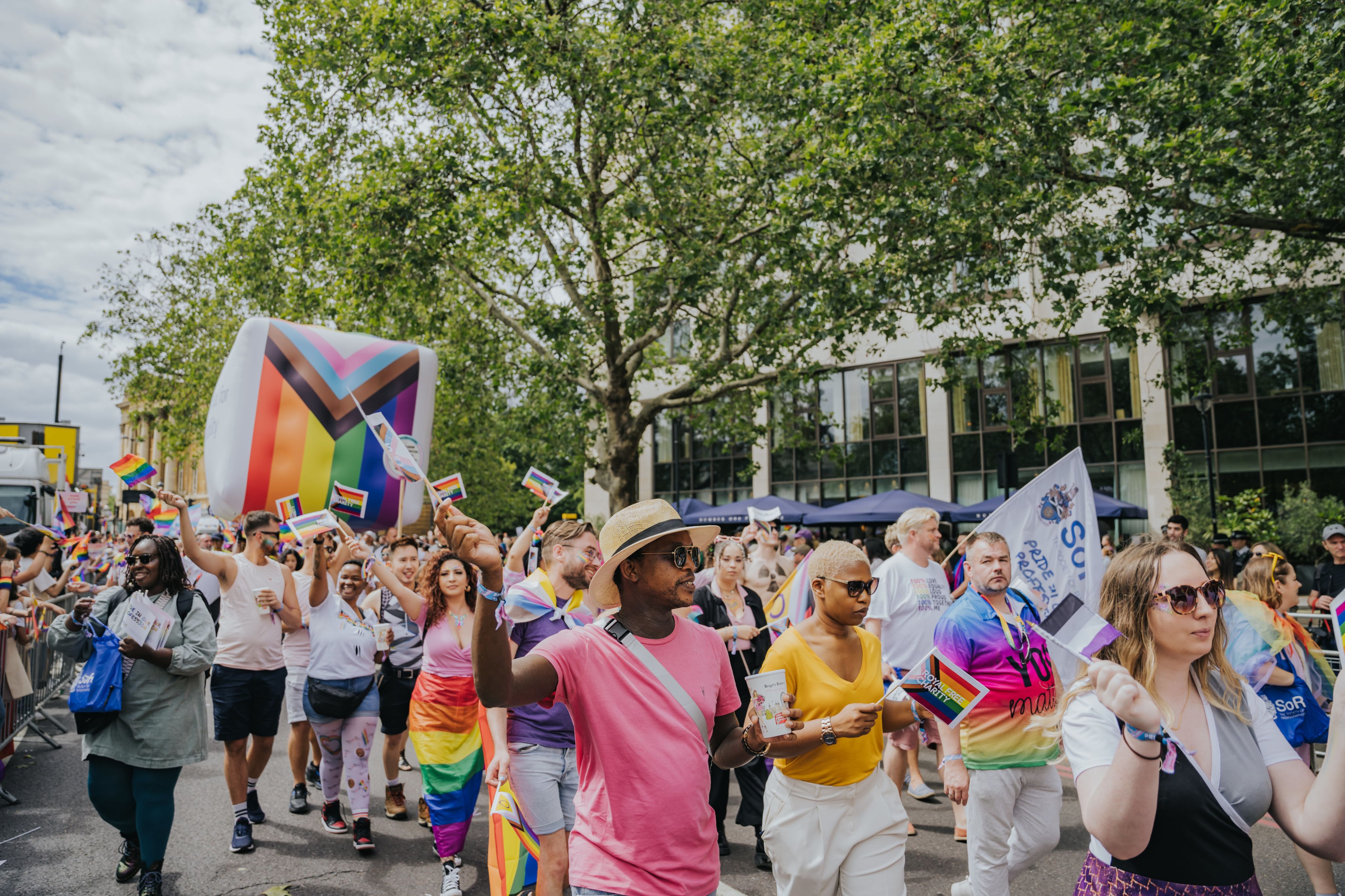 Lots of people walking in procession in the street with rainbow flags